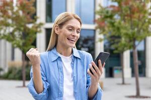 contento riuscito vincitore donna nel blu casuale camicia ricevuto in linea notifica Messaggio su Telefono, maturo attività commerciale donna al di fuori ufficio edificio festeggiare trionfo, con gioia Tenere mano su. foto