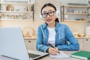 giovane asiatico femmina alunno studiando remoto a casa, ritratto di donna con il computer portatile su in linea apprendimento utilizzando il computer portatile mentre seduta nel cucina a casa foto