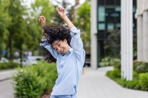 un esuberante giovane donna con Riccio capelli balli con gioia su un urbano marciapiede. sua vivace espressione e spensierato movimento catturare un' senso di la libertà e felicità nel il città ambiente. foto