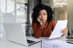 triste deluso donna d'affari dentro ufficio a posto di lavoro guardare a documenti documenti finanziario rapporti, africano americano femmina lavoratore su carta opera depresso infelice con finanziario realizzazioni foto