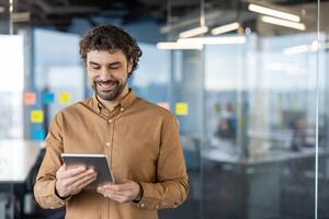 un' sorridente maschio professionale usi un' tavoletta nel un' luminosa, contemporaneo ufficio spazio. il Immagine cattura un' momento di attività commerciale tecnologia uso e lavoro soddisfazione. foto