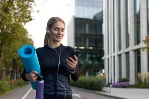 gioioso donna andando per allenamento, atleta con yoga stuoia utilizzando in linea incontri App e comune addestramento. foto