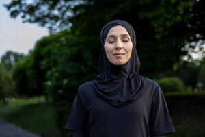 un' giovane donna indossare un' hijab sta all'aperto con sua occhi Chiuso, trasudante un' senso di pace e serenità circondato di natura. foto