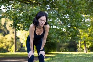 stanco giovane donna in piedi piegato al di sopra di nel parco, riposo e tremante difficile dopo jogging e addestramento. foto