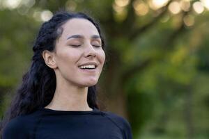 un' ispanico donna si chiude sua occhi con un' soddisfare Sorridi, crogiolarsi nel serenità in mezzo un' naturale verde sfondo. foto