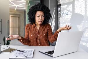 insoddisfatto e deluso triste donna a posto di lavoro guardare a computer portatile, lettura in linea e-mail notifica, donna d'affari irritato e confuso seduta dentro ufficio. foto