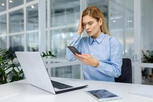 preoccupato libero professionista afferrando testa nel frustrazione mentre controllo tempo su cellulare Telefono e seduta nel coworking. stressato femmina amministratore non adattamento nel tempo telaio per progetto completare. foto