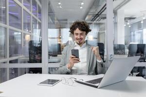 giovane adulto uomo d'affari con Riccio capelli sensazione estatico di successo mentre Lavorando nel un' contemporaneo ufficio ambiente. foto