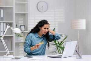 preoccupato ispanico donna d'affari Lavorando a partire dal casa ufficio reagisce per un' frode o errore su sua credito carta. foto