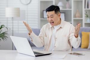 asiatico Lavorando remoto a partire dal casa ufficio con computer portatile, uomo d'affari ricevuto notifica di bene realizzazione risultati, libero professionista soddisfatto con opera gioisce e celebra vittoria e trionfo. foto