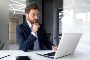 grave giovane uomo d'affari è Lavorando concentrato nel il ufficio su un' il computer portatile e con documenti. foto