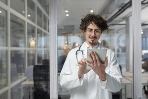 un' medico nel un' bianca laboratorio cappotto e stetoscopio detiene un' tavoletta nel un' medico ufficio. foto