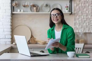 giovane donna prende Appunti nel davanti di il computer portatile a casa. Lavorando a partire dal casa. foto