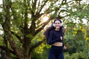 giovane bellissimo ispanico donna in esecuzione con cuffia, donna jogging nel il mattina nel il parco, utilizzando cuffie per ascolta per musica, Audio podcast, e in linea Radio. foto