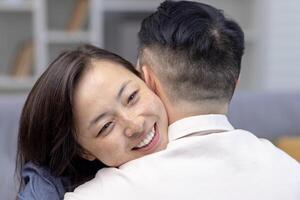 avvicinamento foto. giovane asiatico coppia, famiglia abbracciare insieme. contento viso di giovane donna abbracciare e supporto sua marito, incontra sorridente a casa. foto