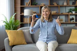un' positivo maturo donna comodamente seduta su un' divano a casa usi un asma inalatore. lei dà un' pollici su, indicando alleviare e sollievo dopo uso. foto