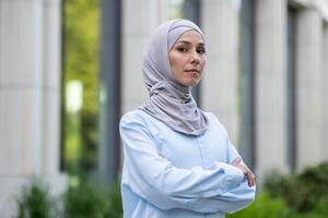 un' professionale donna d'affari nel hijab sta con fiducia all'aperto vicino moderno ufficio edifici. foto