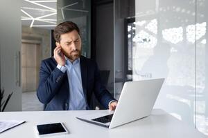 preoccupato giovane uomo seduta nel un' attività commerciale completo da uomo nel il ufficio e Tenere il suo orecchio. si sente disagio, fece una smorfia a partire dal dolore. foto