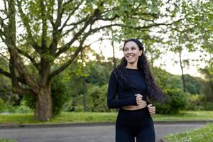 sorridente femmina corridore nel abbigliamento sportivo jogging nel un' verde parco a crepuscolo, raffigurante il gioia di all'aperto esercizio e benessere. foto