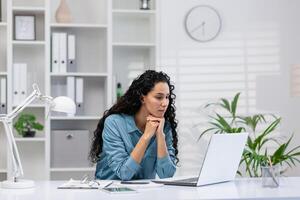 focalizzata ispanico donna Lavorando su sua il computer portatile a partire dal un' ben organizzato casa ufficio, trasudante professionalità e concentrazione. foto