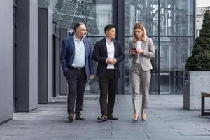 diverso attività commerciale gruppo, tre maschio e femmina lavoratori a piedi e chat discutere piani, al di fuori ufficio edificio foto