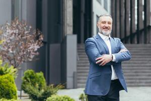 riuscito capo attività commerciale capo uomo guardare a telecamera con braccia attraversato e sorridente, dai capelli grigi uomo d'affari nel attività commerciale completo da uomo foto