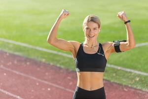 energico donna corridore mostrando forza e successo con un' fiducioso braccio aumentare su un' soleggiato atletico traccia. foto