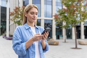 focalizzata donna d'affari sms su Telefono al di fuori moderno ufficio. urbano fondale con spazio per testo. tecnologia e carriera. foto