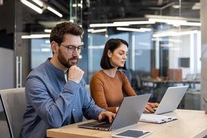 Due focalizzata professionisti Lavorando insieme a un' scrivania con computer portatili nel un' contemporaneo ufficio ambientazione, veicolare collaborazione e lavoro di squadra. foto