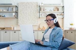 asiatico donna seduta su divano a casa utilizzando il computer portatile per orologio educativo , alunno studiando remoto in linea. foto