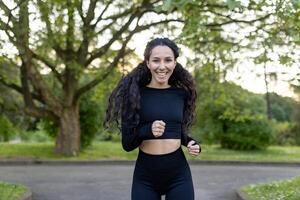 un' gioioso donna con un' luminosa Sorridi gode un' correre nel il lussureggiante verdura di un' pubblico parco, incarnando Salute e fitness. foto