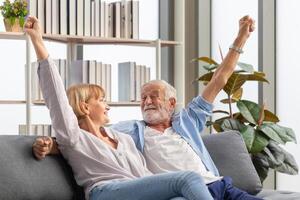 anziano coppia rallegrare su loro preferito squadra mentre Guardando calcio gioco nel vivente camera, anziano donna e un' uomo rilassante su accogliente divano a casa, contento famiglia concetti foto