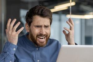 adulto maschio nel un' blu camicia sensazione stressato e infastidito mentre di fronte computer problemi nel un' moderno ufficio ambiente. foto