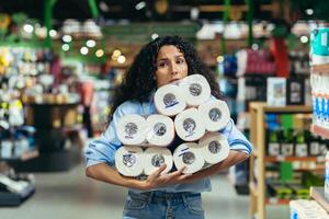 spaventato donna acquirente nel supermercato acquista gabinetto carta, latino americano donna nel crisi e mancanza di merce sceglie scarso merce foto