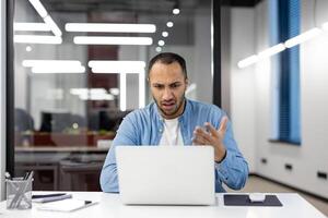 giovane maschio professionale nel un' moderno ufficio ambientazione apparendo stressato e confuso mentre Lavorando su il suo computer portatile, visualizzazione un' cartello di attività commerciale sfide. foto