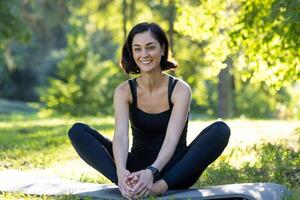 soddisfare donna praticante consapevolezza durante all'aperto yoga sessione nel un' tranquillo parco, circondato di lussureggiante verde. foto