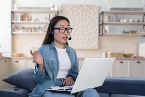 giovane bellissimo asiatico donna studiando remoto seduta nel vivente camera su divano, femmina alunno foto