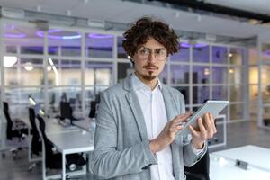 un' giovane maturo uomo d'affari con Riccio capelli si concentra su il suo tavoletta mentre Lavorando nel un' contemporaneo ufficio impostare, incarnando professionalità. foto