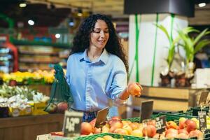 sorridente latino americano attività commerciale donna sceglie e acquista fresco mele, frutta nel il supermercato foto