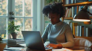 nero donna si siede a un' spazio di lavoro profondamente focalizzata su utilizzando sua il computer portatile foto