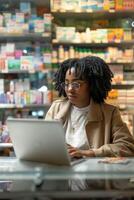 giovane nero donna è utilizzando un' il computer portatile per gestire un' farmacia memorizzare foto