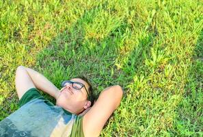 giovane uomo con bicchieri mentito su erba godendo vacanza dopo studiando molto contento foto