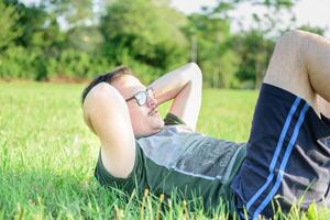 giovane uomo con bicchieri e verde maglietta fare sit-up e esercizio nel parco foto