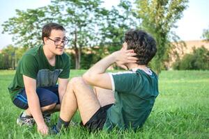 Due amici fare esercizio e sit-up con verde maglietta nel parco foto
