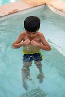 contento indiano ragazzo nuoto nel un' piscina, ragazzo indossare nuoto costume lungo con aria tubo durante caldo estate vacanze, bambini ragazzo nel grande nuoto piscina. foto