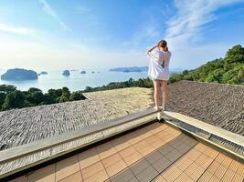 un' donna gode un' sereno mattina camminare lungo un' terrazza con un' sbalorditivo panoramico Visualizza di lontano isole sotto un' luminosa sole, in mostra il Perfetto miscela di rilassamento e naturale bellezza foto