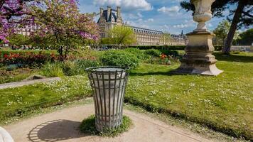 vuoto metallo spazzatura può nel un' vivace città parco durante primavera con fioritura alberi, tulipani, e storico architettura nel il sfondo, ideale per terra giorno concetti foto