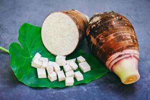 radice di taro con metà e cubetti di fetta su foglia di taro e sfondo di legno, radice di taro organica cruda fresca pronta da cucinare foto