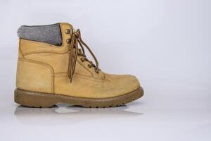 uno logoro vecchio giallo escursioni a piedi il trekking pizzo stivali isolato su bianca lucido superficie con bellissimo riflessione effetto. secondo mano turista a piedi scarpe. lato Visualizza. copia spazio. bianca sfondo. foto