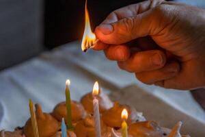 Uomini mano Tenere fiammiferi e illuminazione colorato candele su il grande fatti in casa cioccolato compleanno torta, decorato con meringhe e frustato crema. avvicinamento. selettivo messa a fuoco. foto